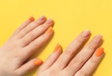 Mãos com unhas pintadas de laranja sobre superfície amarela