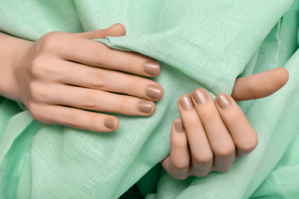 Mãos com unhas pintadas de tom pastel sobre tecido verde