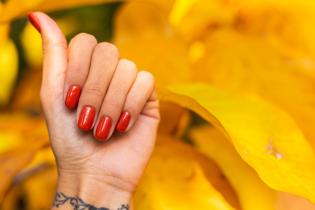 Mãos com unhas pintadas de laranja sobre superfície amarela