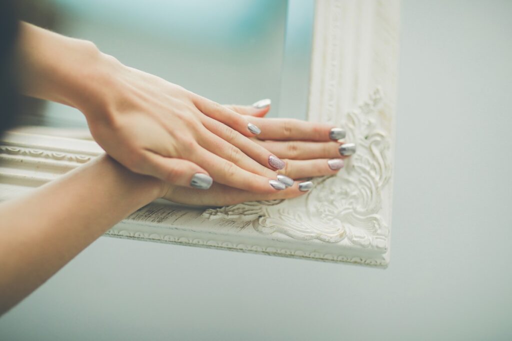 Mãos com unhas pintadas de tom metálico sobre moldura de quadro branco.