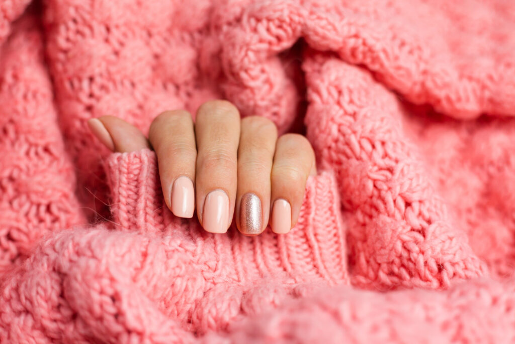 Mãos com unhas pintadas de tom rosáceo sobre tecido rosa