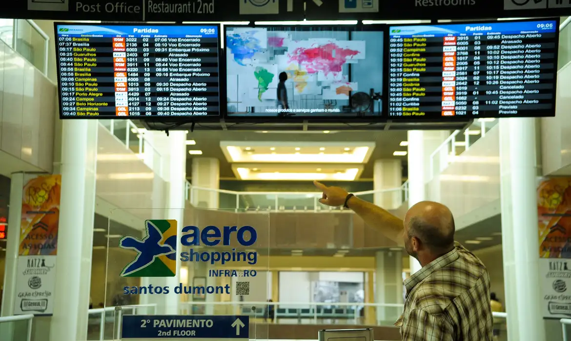 Imagem de um idoso no aeroporto apontando para a tela de embarque