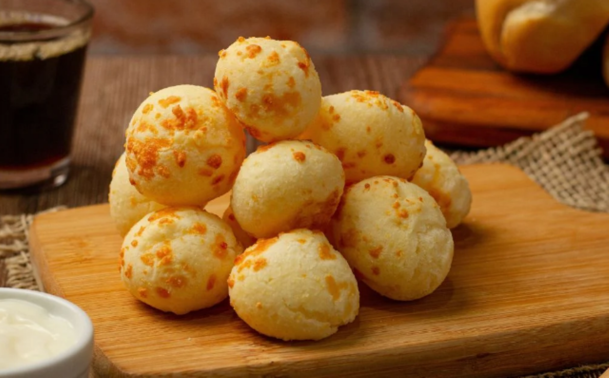Deliciosos pães de queijo mineiros crocantes por fora e macios por dentro, servidos sobre uma tábua de madeira.