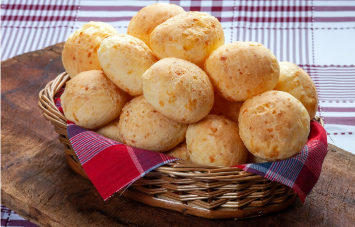 Uma cesta cheia de pães de queijo mineiros dourados, com uma toalha de mesa quadriculada ao fundo.