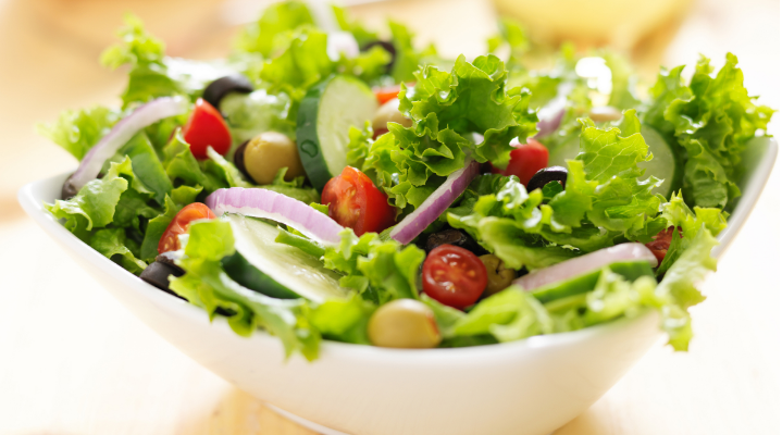 Salada verde fresca com alface, pepino, tomate cereja, cebola roxa, azeitonas e tempero leve, servida em tigela branca.