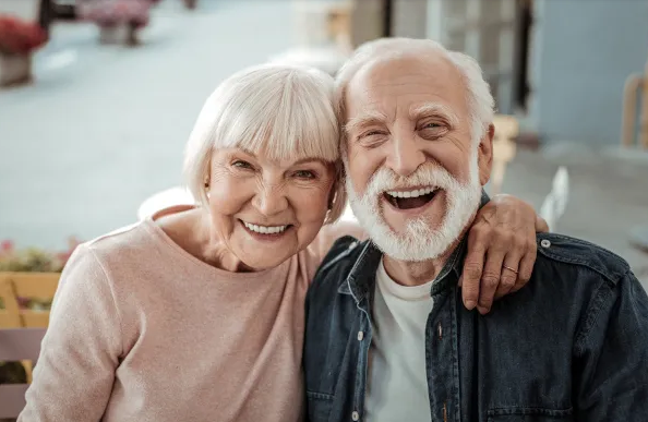 Casal idoso sorrindo e abraçado ao ar livre, transmitindo alegria e cumplicidade.