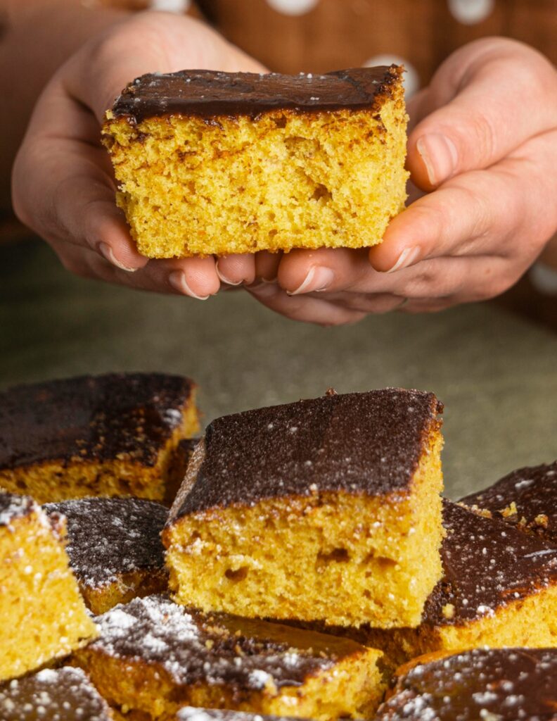 Bolo de fubá fofinho com cobertura de chocolate sendo segurado, representando dicas para fazer o bolo perfeito.