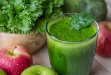 Suco verde de couve com maçã em um copo, com maçãs e folhas de couve ao fundo.