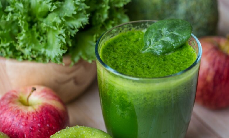 Suco verde de couve com maçã em um copo, com maçãs e folhas de couve ao fundo.