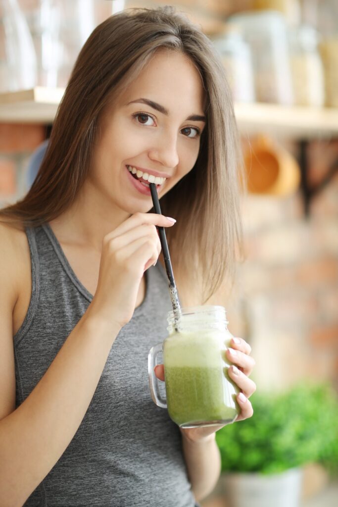 Mulher sorrindo enquanto toma suco verde de couve com maçã, simbolizando os benefícios dessa bebida saudável.