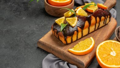 Bolo de laranja fofinho com calda de chocolate e rodelas de laranja sobre uma tábua de madeira.