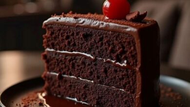 Fatia de bolo de chocolate molhadinho com cobertura cremosa e cereja no topo.