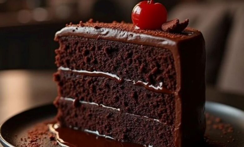 Fatia de bolo de chocolate molhadinho com cobertura cremosa e cereja no topo.