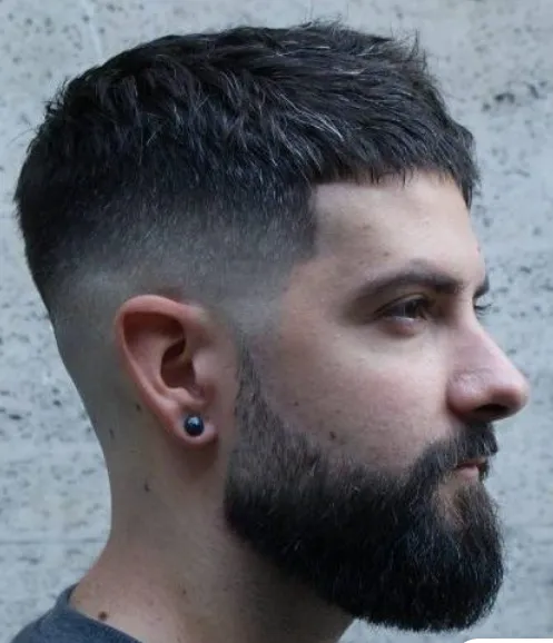 Homem com cabelo curto e barba espessa, estilo fade, em perfil.