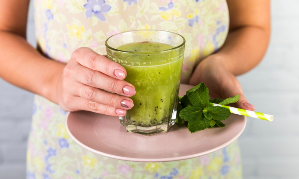 Mulher segurando um copo de suco verde com hortelã, ilustrando os benefícios para o sistema digestivo.