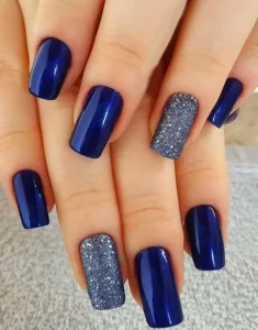 Unhas decoradas com esmalte azul e detalhes em glitter prateado, tendência de 2024.