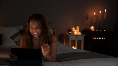 Mulher sorrindo enquanto assiste algo no tablet à noite, em um ambiente iluminado por velas