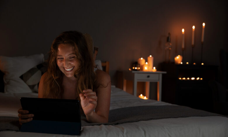 Mulher sorrindo enquanto assiste algo no tablet à noite, em um ambiente iluminado por velas