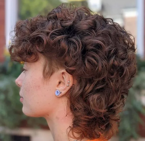 Pessoa com cabelo cacheado e corte mullet, visível de perfil.