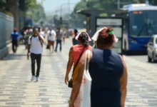 Pessoas caminhando nas ruas durante uma onda de calor, com destaque para as roupas leves e gestos de desconforto devido ao calor.