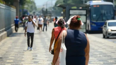 Pessoas caminhando nas ruas durante uma onda de calor, com destaque para as roupas leves e gestos de desconforto devido ao calor.