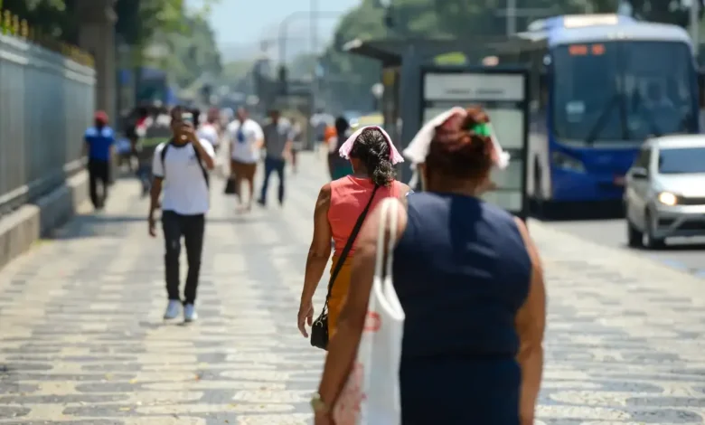 Pessoas caminhando nas ruas durante uma onda de calor, com destaque para as roupas leves e gestos de desconforto devido ao calor.