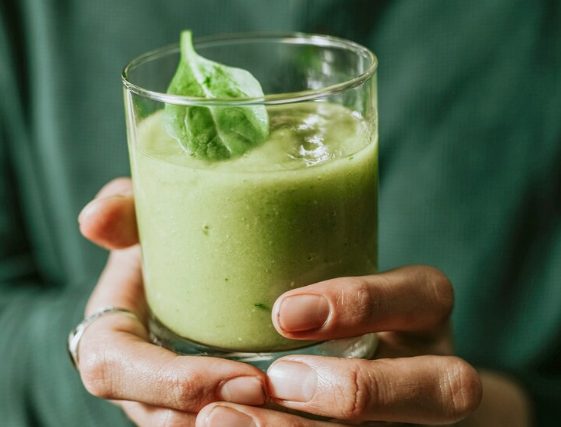 Pessoa segurando um copo de smoothie verde com folha de espinafre.