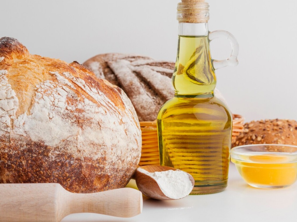 Ingredientes para pão caseiro: pães rústicos, azeite, farinha e mel sobre a mesa.