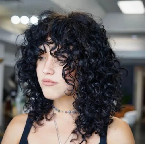 Pessoa com cabelo cacheado e corte estilo wolf cut, com franjas longas e volumosas.