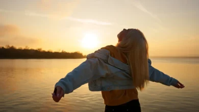 Pessoa de braços abertos, olhando para o sol ao amanhecer, transmitindo uma sensação de gratidão e liberdade