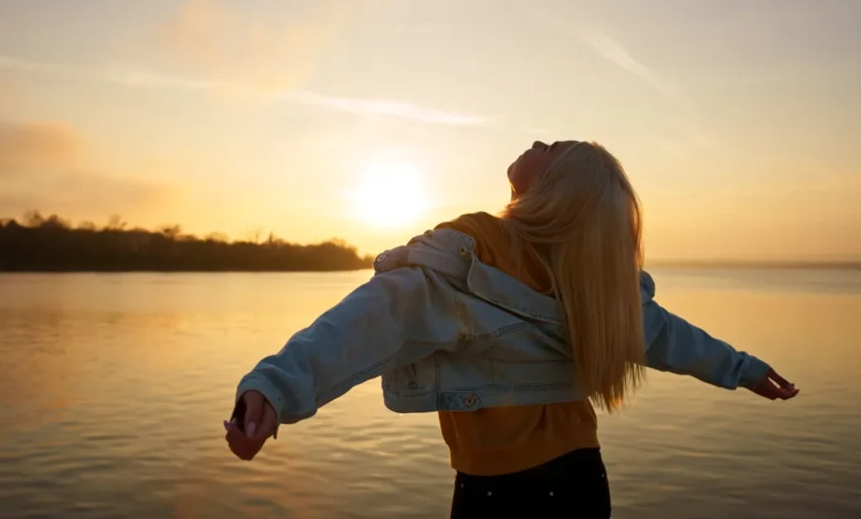 Pessoa de braços abertos, olhando para o sol ao amanhecer, transmitindo uma sensação de gratidão e liberdade