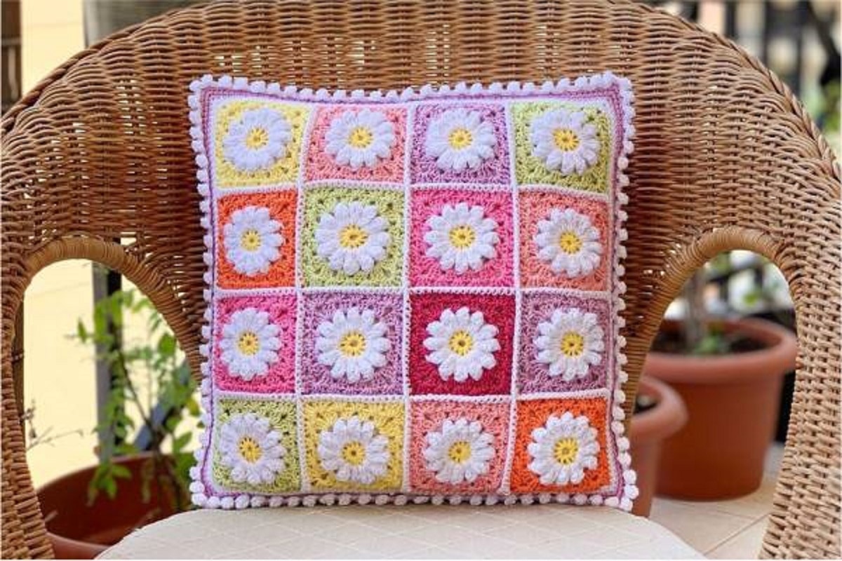 Almofada de crochê retangular com quadrados coloridos e aplicação de flores brancas em relevo.