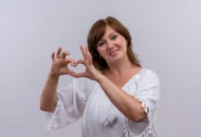 Mulher sorrindo e fazendo um coração com as mãos, simbolizando amor-próprio e autoestima.