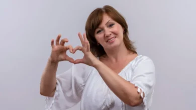 Mulher sorrindo e fazendo um coração com as mãos, simbolizando amor-próprio e autoestima.