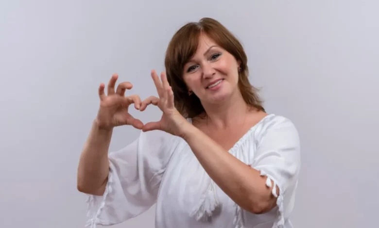 Mulher sorrindo e fazendo um coração com as mãos, simbolizando amor-próprio e autoestima.