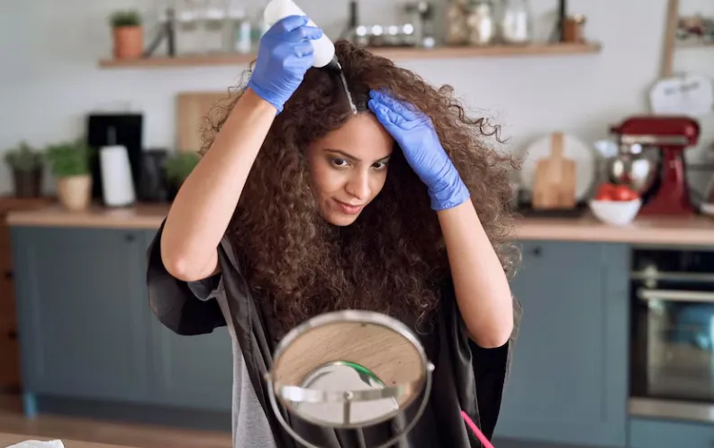  Mulher com cabelo cacheado tingindo os fios sozinha em casa.