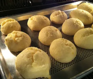 Pãezinhos de tapioca dourados assando em uma assadeira perfurada