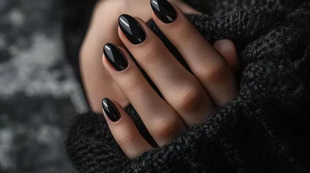 Unhas esmaltadas de preto brilhante, segurando um suéter escuro, com um fundo suave e desfocado.