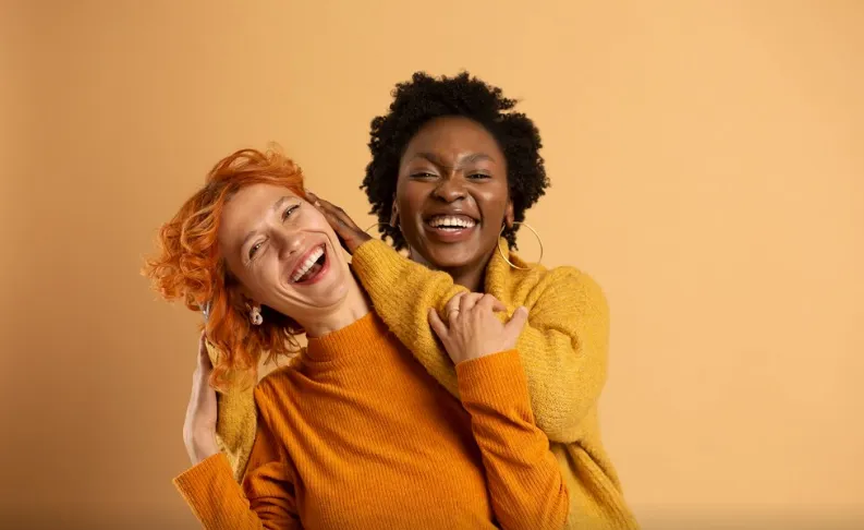 Duas amigas sorrindo e se abraçando, transmitindo alegria e positividade para uma mensagem de boa noite.