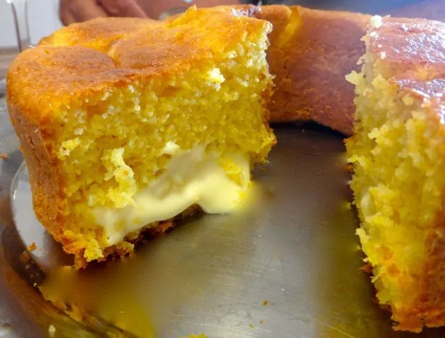 Bolo de milho fofinho com recheio cremoso de queijo derretido, servido em uma bandeja.