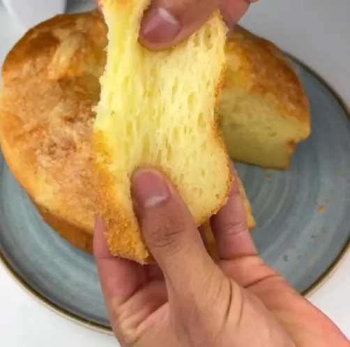 Bolo de polvilho com queijo sendo puxado, mostrando sua textura macia e elástica.