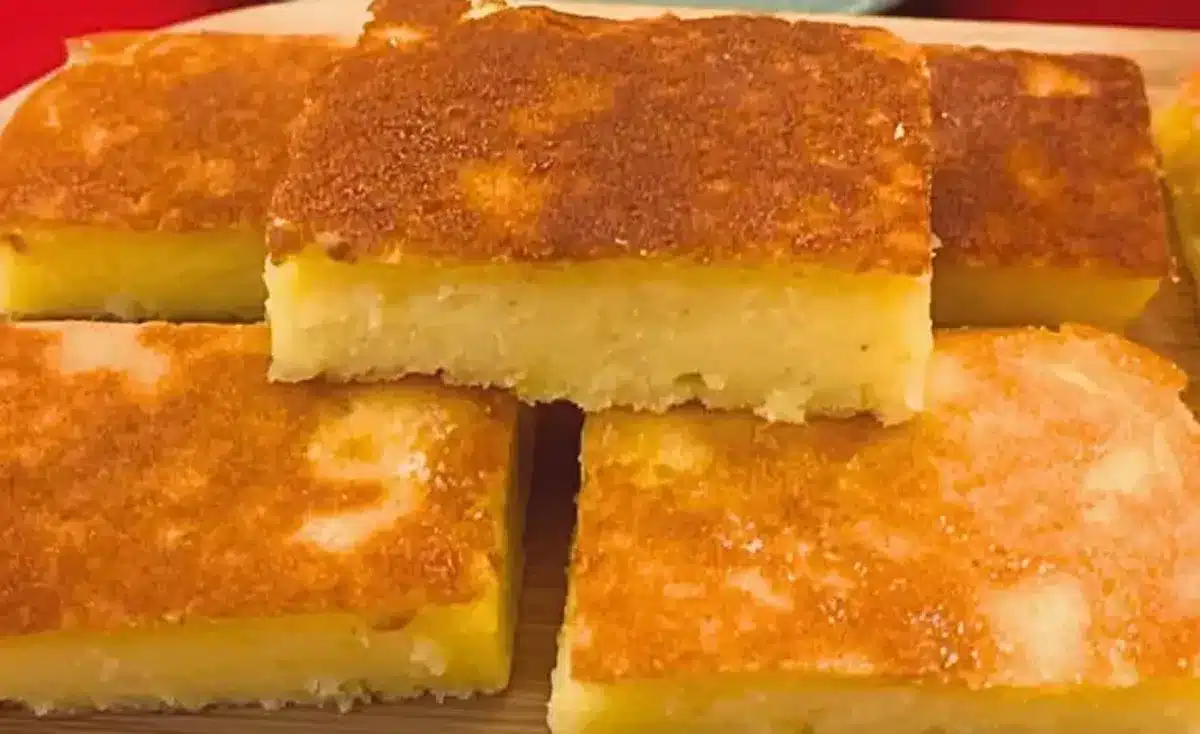 Bolo de mandioca cremoso da roça, cortado em pedaços e com uma crosta dourada e macia.