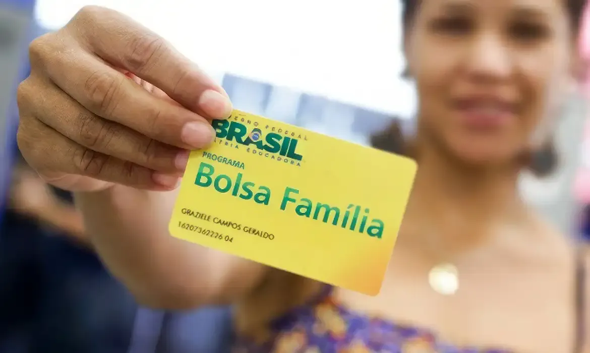 Mulher segurando um cartão do Bolsa Família, simbolizando o pagamento do benefício.