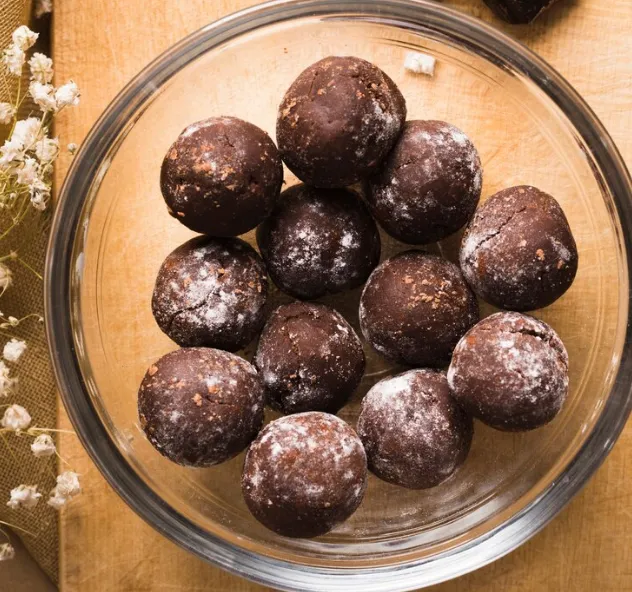 Brigadeiros fit com cacau servidos em um bowl de vidro sobre uma tábua de madeira.