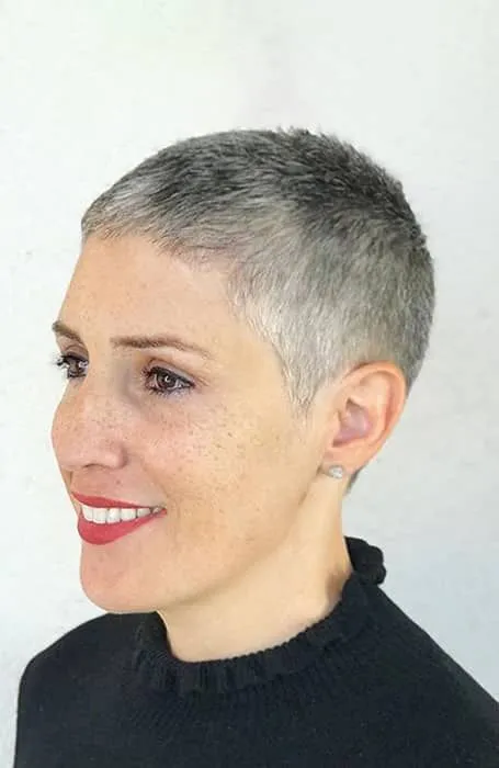 Imagem de uma mulher com corte buzzcut, cabelo muito curto e cinza, sorrindo e usando uma blusa preta.