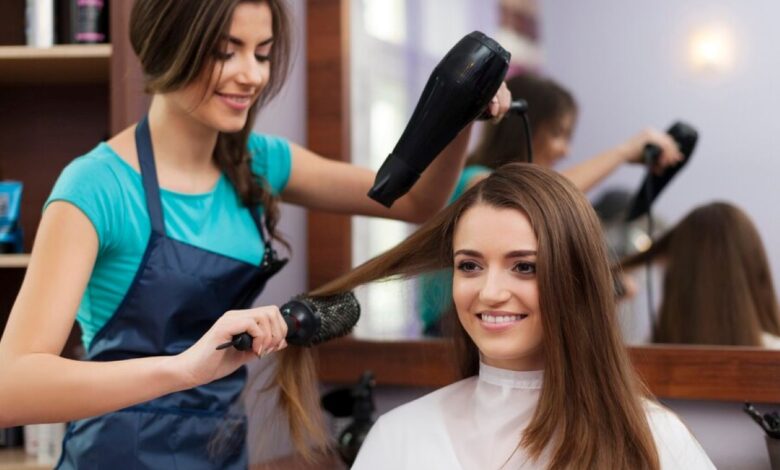 Cabeleireira usando secador e escova para fazer um penteado feminino.