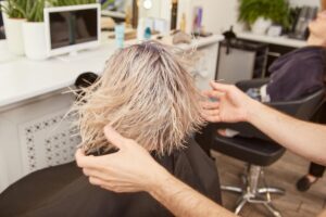 Profissional de cabelo aplicando um tratamento em cabelo grisalho, em um salão de beleza.