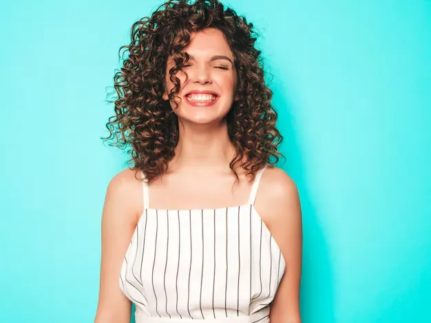 Mulher sorrindo com cabelo cacheado volumoso, usando um vestido listrado em branco e preto.