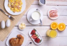 Café da manhã nutritivo com croissant, frutas, ovos mexidos, bacon, leite e suco de laranja.