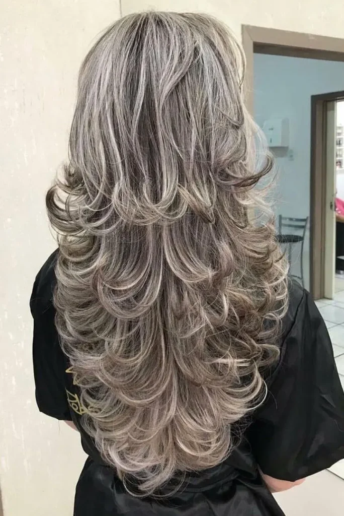 Cabelo longo com camadas volumosas e curvadas, com tons platinados.